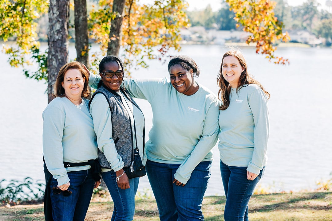 four women smiling for a picture in front of a lake